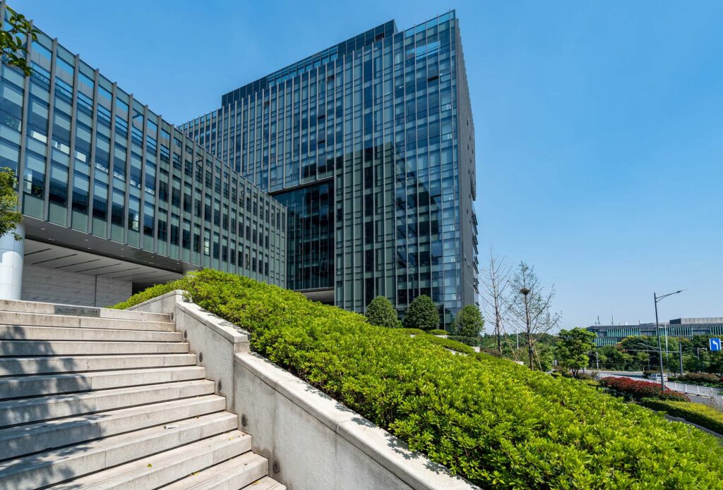 Nowoczesny biurowiec ze szkła otoczony roślinnością od Giardini Polska, zgodny z ESG i ekologicznym designem.